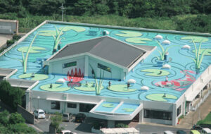 介護施設の鳥瞰図。青い屋根と複数の出入口を備えた大型施設建物の俯瞰景観。